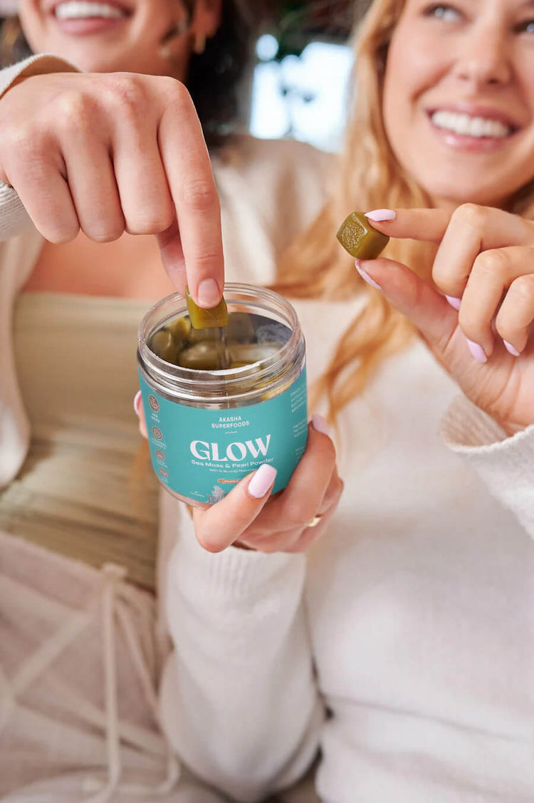 Two people holding and taking gummies from a jar labeled 'Glow.'