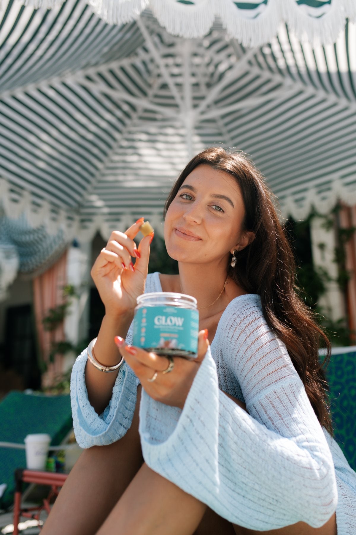Customer under a striped umbrella holding a jar of GLOW gummies