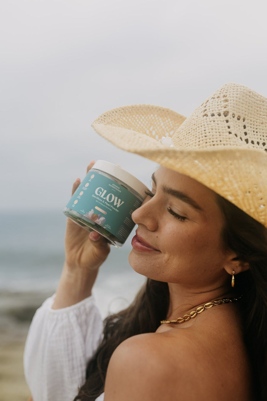 Customer in a straw hat holding a jar of GLOW gummies to her cheek at the beach