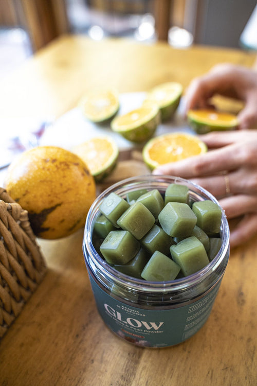 Open jar of GLOW gummies on a wooden table with halved oranges