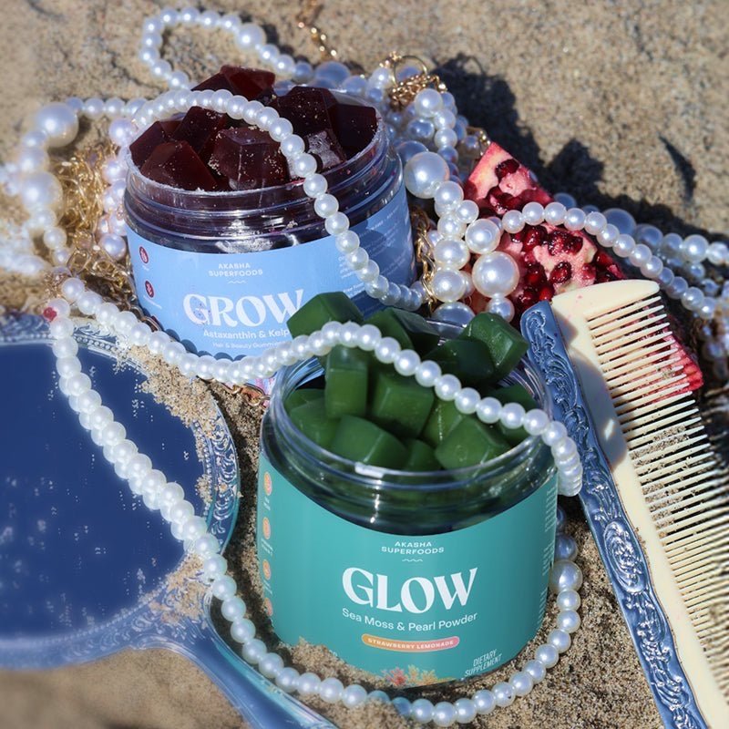 Akasha Superfoods GROW and GLOW gummy jars on sand with shells, pearls and a mirror.
